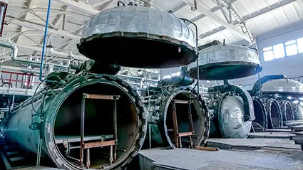 Fila de autoclaves industriales con tapas abiertas en una planta de fabricación