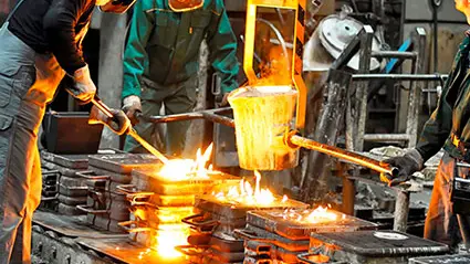 Operarios en fundición vertiendo metal fundido en una línea de moldes industriales