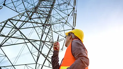 Técnico con casco y radio inspeccionando una torre de transmisión eléctrica